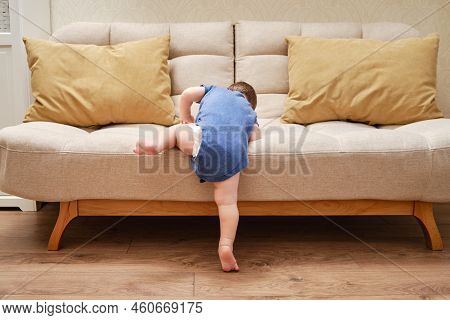 Toddler Baby Climbs On The Sofa. Child Boy Learning To Get Off The Bed. Kid Age One Year