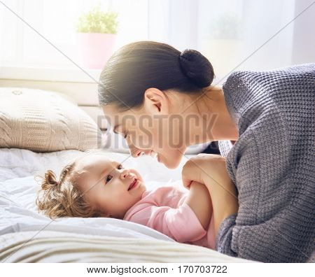 Happy loving family. Young mother are playing with her baby girl in the bedroom. Mom and child are having fun on the bed.