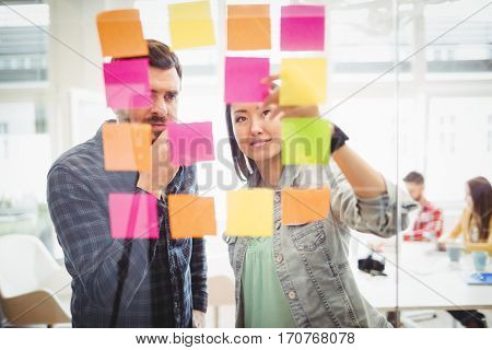 Creative business people looking at multi colored sticky notes on glass in meeting room at creative office