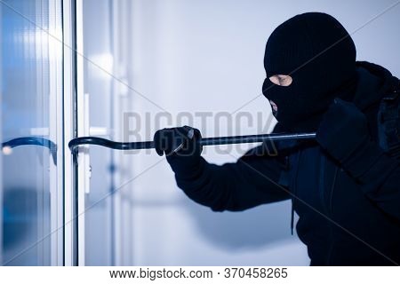 Home Security Concept. Burglar In Action Trying To Break Into The House Using Crowbar, Side View