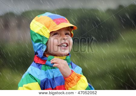 Pikkupoika nauttia pukeutunut rainbow värillinen sadetakki sadetta