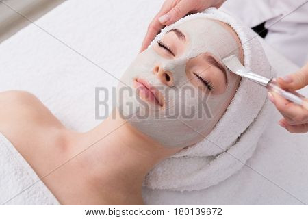 Face peeling mask, spa beauty treatment, skincare. Woman getting facial care by beautician at spa salon, side view, close-up