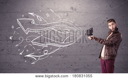 A hipster guy opening his point of view through looking a vintage camera concept with illustratied drawn arrows on urban wall