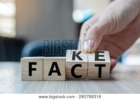 Business Man Hand Holding Wooden Cube With Flip Over Block Fake To Fact Word On Table Background. Ne