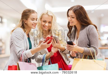 sale, consumerism, technology and people concept - happy young women with smartphones and shopping bags in mall