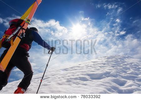  Ski mountaineer walking up along a steep snowy ridge with the skis in the backpack. In background a dramatic sky. Concepts: adventure, achievement, courage, determination, extreme sport