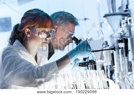 Health care researchers working in life science laboratory. Young female research scientist and senior male supervisor preparing and analyzing microscope slides in research lab.