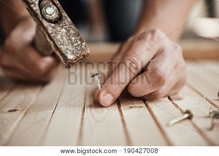 Carpenter with hammer and nails repairing part of furniture on the floor. Concept of construction and woodwork.