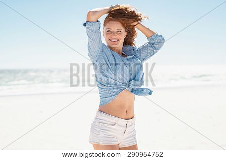 Happy beautiful woman enjoy the breeze on beach laughing. Portrait of carefree mature woman with the wind in her red hair relaxing at sea. Young smiling girl enjoying wind at sea in a sunny day.