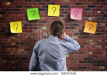 Choice and decisions: businessman thinking with question marks written on adhesive notes stuck to a brick wall