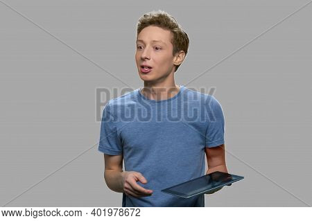 Teenage Boy Speaking While Holding Pc Tablet. Young Software Engineer Giving A Lecture On Gray Backg