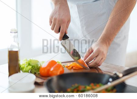 cooking, food and home concept - close up of male hand cutting pepper on cutting board at home