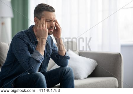 Stressed Middle-aged Bearded Man Having Headache, Sitting On Sofa At Home And Rubbing His Temples, C