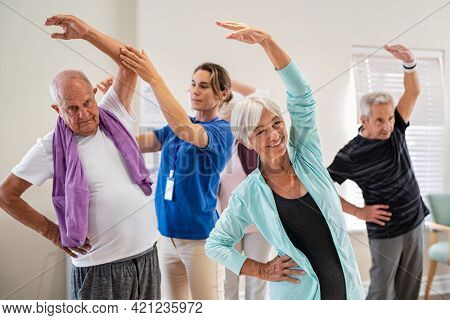 Active seniors doing exercise with physiotherapist at nursing home gym. Trainer helping elderly man and old woman exercising at home. Retired people doing stretching exercises at retirement community.