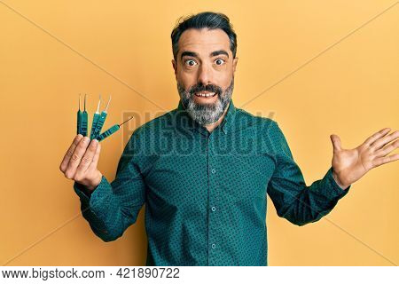 Middle age man with beard and grey hair holding picklock to unlock security door celebrating achievement with happy smile and winner expression with raised hand 