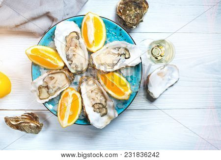 Fresh Oysters close-up on blue plate, served table with oysters, lemon and ice. Table top view. Healthy sea food. Fresh raw Oyster dinner in restaurant. Gourmet food. Tabletop