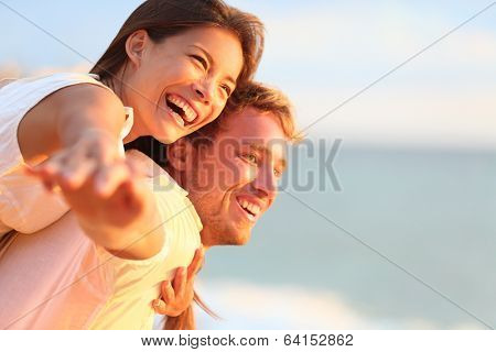 Beach couple laughing in love romance on travel honeymoon vacation summer holidays romance. Young happy people, Asian woman and Caucasian man embracing outdoors on tropical beach in casual wear.