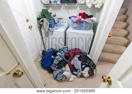 Cluttered messy laundry room with piles of clothes needing to be washed.  