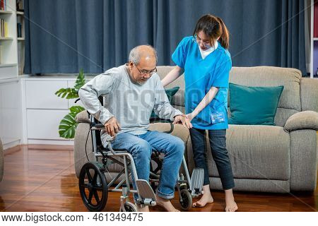 Asian Nurse Assisting Helping Senior Man Patient Get Up From Wheelchair For Practice Walking At Home