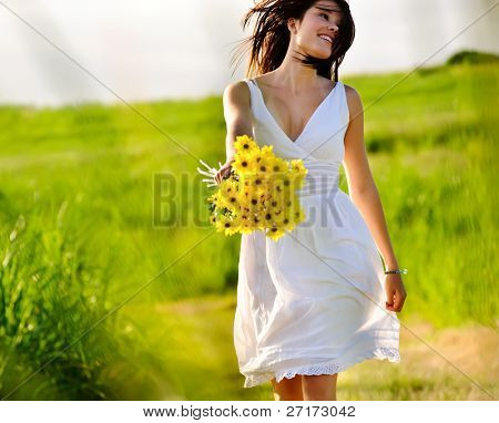 Sincera pulando despreocupada adorável mulher no campo com flores, pôr do sol de Verão.