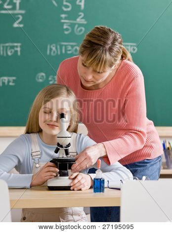 Teacher helping student adjust microscope in school science classroom