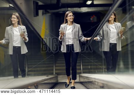 A Happy Businesswoman Is Ascending The Escalator And Going To Her Office. An Elegant Young Woman Goi