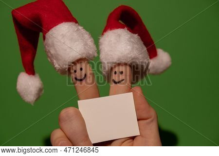 Fingers Dressed In Santa-claus Red-white Hats. Two Happy Finger Smileys Faces Holding Empty Paper No