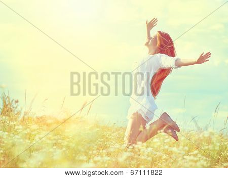 Beauty Girl Outdoors enjoying nature. Beautiful Teenage Model girl in white dress jumping on summer Field with blooming wild flowers, Sun Light. Free Happy Woman. Toned in warm colors