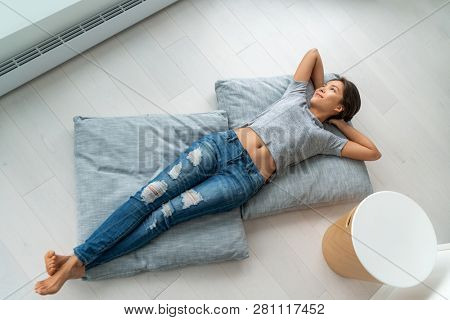 Home lifestyle happy Asian woman relax lying down on living room floor pillows relaxing contemplative looking at windows. New condo apartment satisfaction homeowner young girl enjoying house.