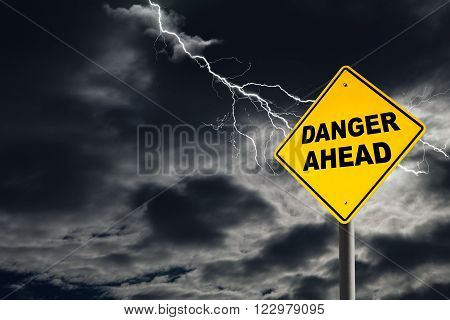 Danger Ahead road sign against a dark cloudy and thunderous sky. Conceptually warning of danger ahead.