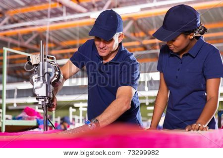 senior textile worker teaching new employee about cutting material