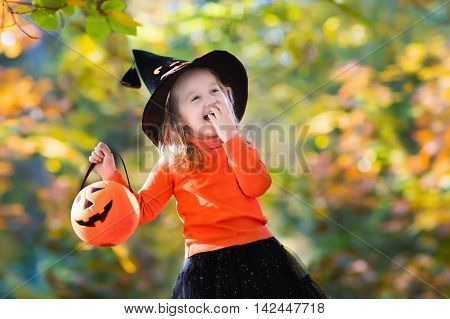 Little girl in witch costume playing in autumn park. Child having fun at Halloween trick or treat. Kids trick or treating. Toddler kid with jack-o-lantern. Children with candy bucket in fall forest.