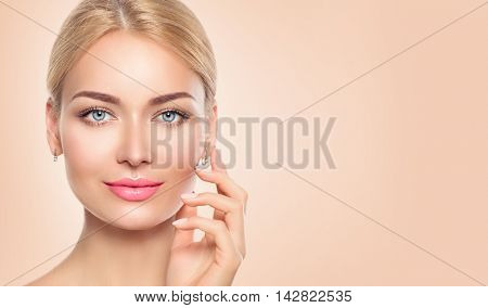 Beauty Woman face closeup Portrait. Beautiful Spa Girl Touching her Face and smiling. Perfect Fresh Skin. Pure Beauty Model Female looking at camera. Youth and Skin Care Concept. Beige background