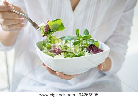 Close up shot of a woman holding a plate of fresh green salad in the beautiful morning light. She's holding a fork and she's about to eat the vegetarian food. Healthy eating and diet concept.