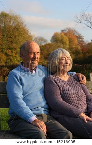 Mature couple seated in a park in the fall relaxed watching grandchildren playing.