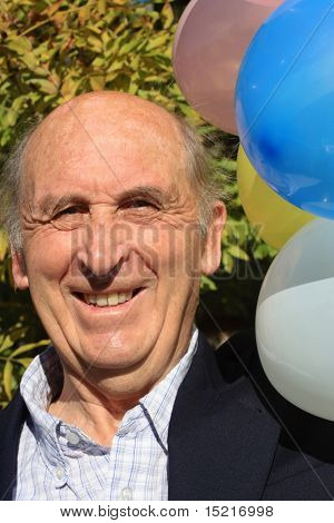 Senior mature man enjoying a retirement or birthday party with colorful balloons and leaves.