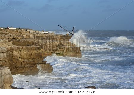 Winter storm in Portland Dorset with waves breaking against the coastline and a boat winch in the distance.