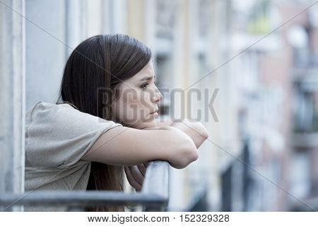 young sad beautiful woman suffering depression looking worried and wasted on home balcony with an urban view in lonely depressed and desperate female concept