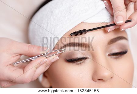 Permanent makeup. Beautiful young woman gets eyebrow correction procedure. Young woman tweezing her eyebrows in beauty saloon. Young woman plucking eyebrows with tweezers close up