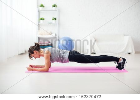 Fit girl in plank position on mat at home in the living room exercise for back spine and posture Concept pilates fitness sport