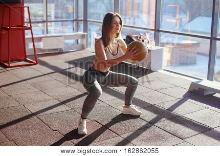 Young Woman Doing Squats With Medicine Ball In Gym