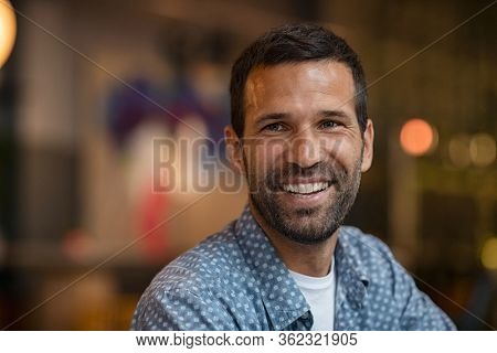 Portrait of happy mid adult man with beard. Close up of successful young entrepreneur in casual smiling and looking away. Hopeful business man smiling sitting in cafe; future and vision concept.