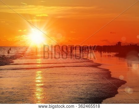 group of silhouetted people on public beach over orange colored sunset sky in Siesta key, Sarasota, Florida