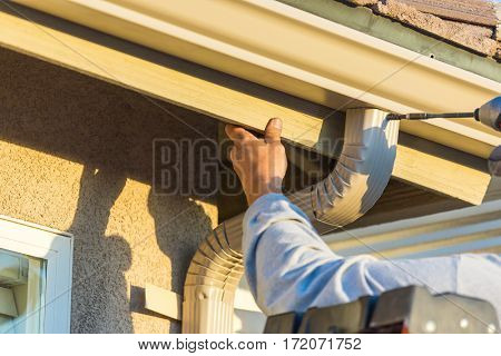 Worker Attaching Aluminum Rain Gutter and Down Spout to Fascia of House.