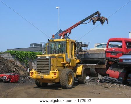 A Truck Lifting A Car Wreck Into Press