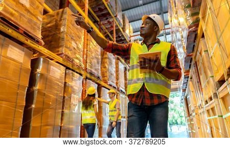 Portrait african black warehouse supervisor standing with digital tablet check stock in large warehouse distribution center with colleague worker in background. Business warehouse and logistic concept