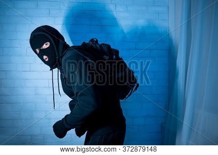 Burglary Concept. Sneaky And Scared Intruder Wearing Black Balaclava Hat Lurking In The Dark, Lookin