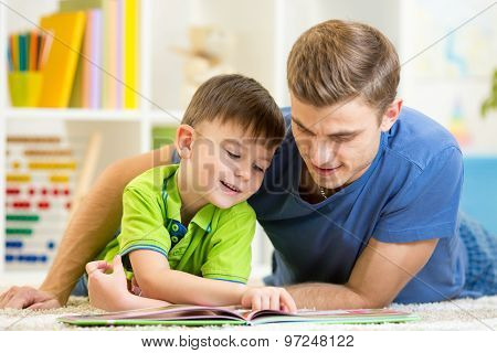 Father and son read together sitting on the floor. Kid reading story book with his dad at home.