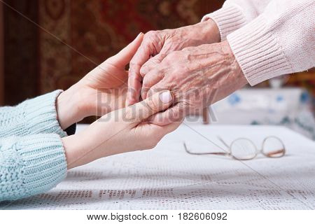 Care is at home of elderly. Senior woman with their caregiver at home. Concept of health care for elderly old people, disabled. Elderly woman holding hands closeup. Space for text white background.