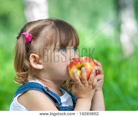 Little girl portrait eating red apple outdoor